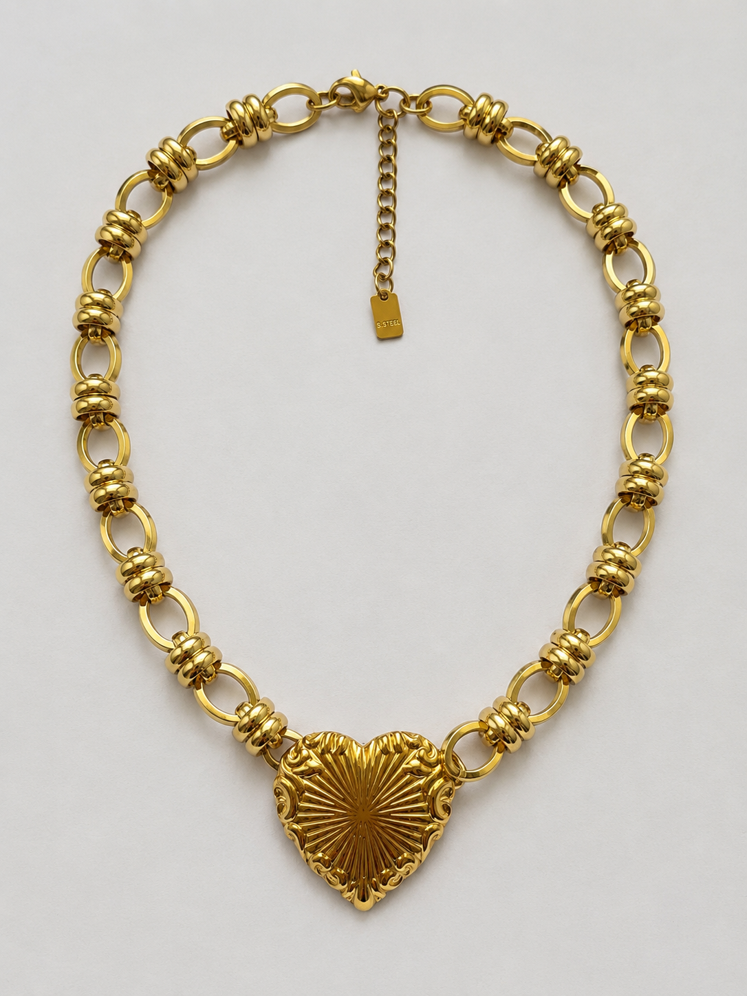Collier Alina doré, cœur à rayons de soleil en relief, chaîne à maillons ovales et anneaux striés, packshot sur fond clair