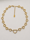 Collier Athéna en packshot, cœurs ajourés dorés, cœurs du centre pavés de zircons, fermoir mousqueton, plaquette S.Steel