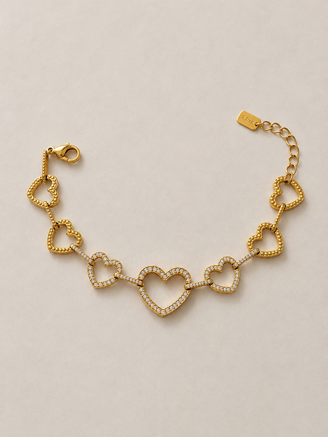 Athéna, bracelet de cœurs dorés ajourés sertis de zircons, packshot sur fond beige