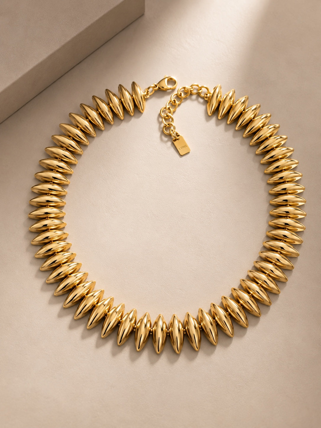 Alicia, collier doré à grains bombés, packshot sur fond beige