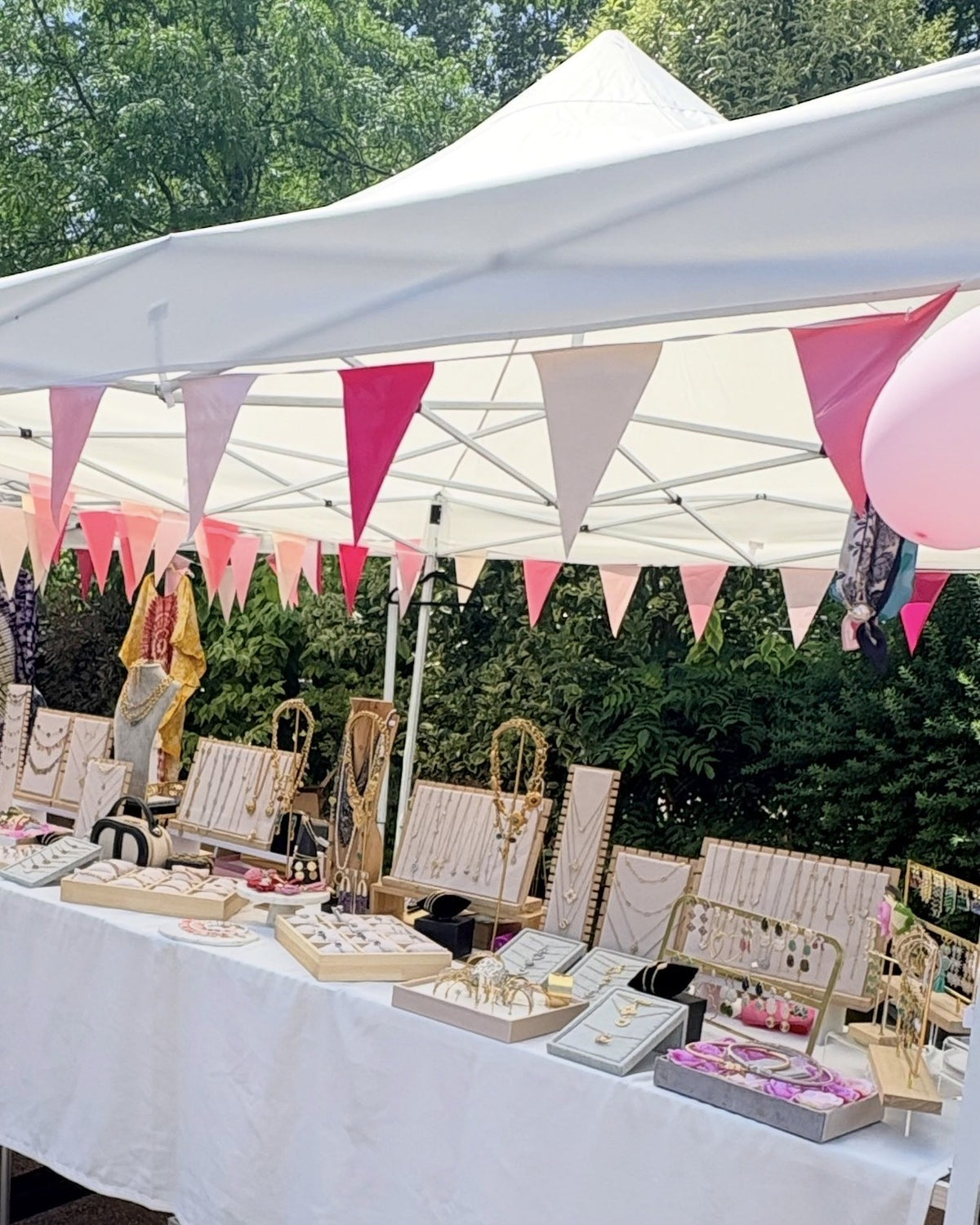 Le stand LOVELYNAW sur un marché : tente blanche, fanions roses et présentoirs de bijoux dorés